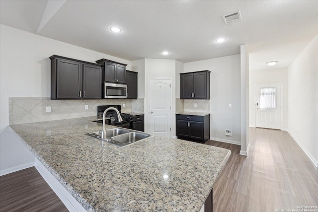 kitchen with tasteful backsplash, sink, hardwood / wood-style flooring, kitchen peninsula, and light stone countertops