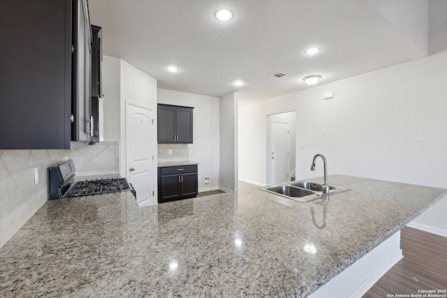 kitchen featuring tasteful backsplash, sink, light stone counters, kitchen peninsula, and gas stove