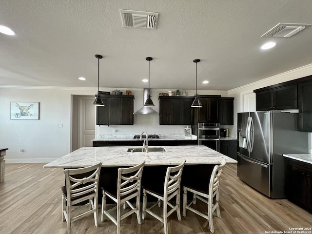 kitchen with light wood-type flooring, stainless steel fridge, ornamental molding, and a center island with sink