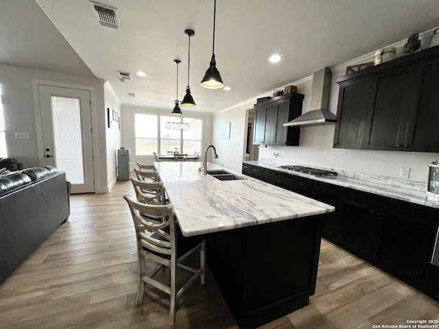 kitchen with pendant lighting, sink, wall chimney exhaust hood, a center island with sink, and stainless steel gas stovetop