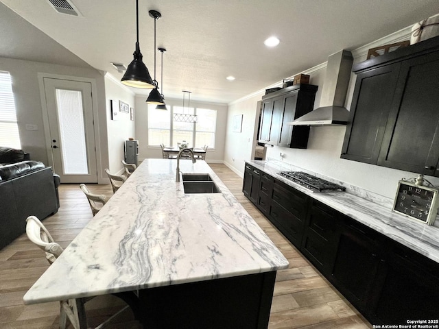 kitchen featuring sink, hanging light fixtures, a large island with sink, stainless steel gas cooktop, and wall chimney exhaust hood