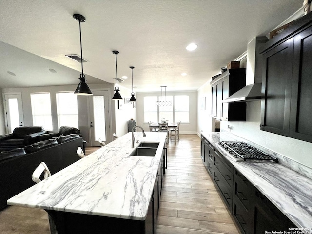 kitchen with a spacious island, sink, decorative light fixtures, light wood-type flooring, and wall chimney range hood