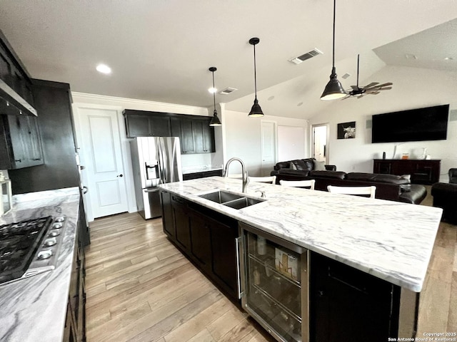 kitchen with lofted ceiling, sink, a center island with sink, stainless steel fridge with ice dispenser, and decorative light fixtures