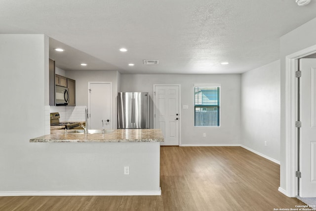 kitchen featuring tasteful backsplash, light wood-type flooring, stainless steel refrigerator, kitchen peninsula, and range with electric cooktop