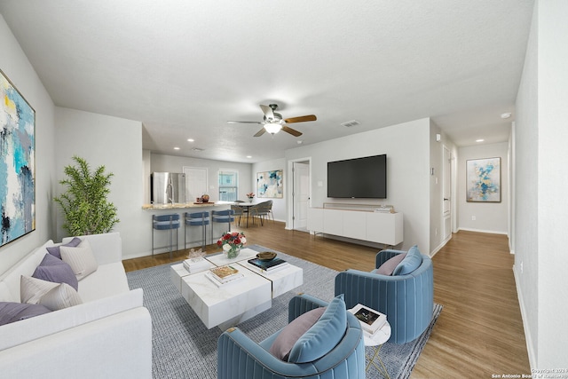 living room with ceiling fan, a textured ceiling, and light wood-type flooring