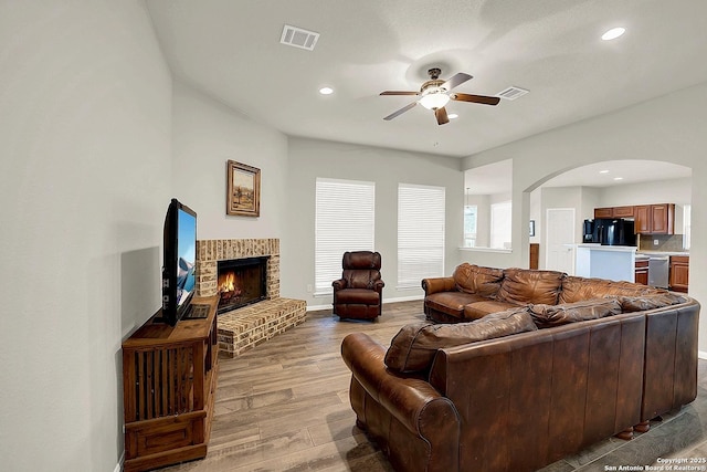 living room with a brick fireplace, light hardwood / wood-style floors, and ceiling fan