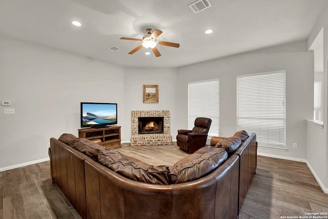 living room with wood-type flooring, ceiling fan, and a fireplace