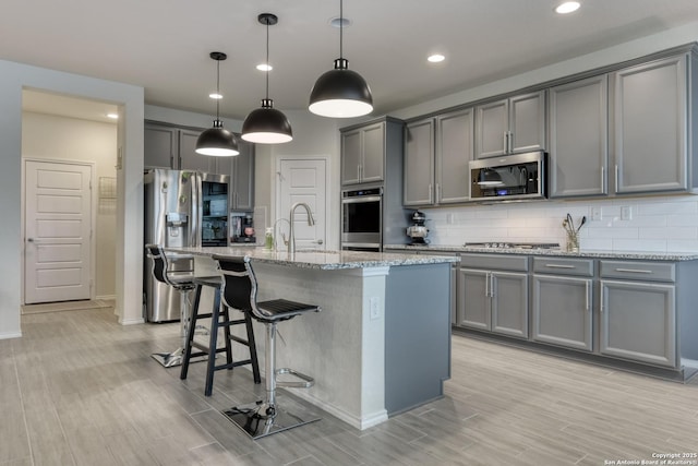 kitchen with stainless steel appliances, light stone countertops, sink, and pendant lighting