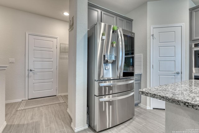 kitchen featuring light stone counters, stainless steel appliances, and gray cabinetry