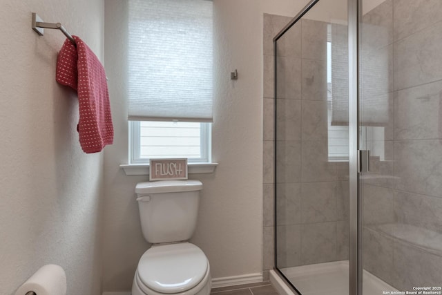 bathroom featuring a shower with door and toilet