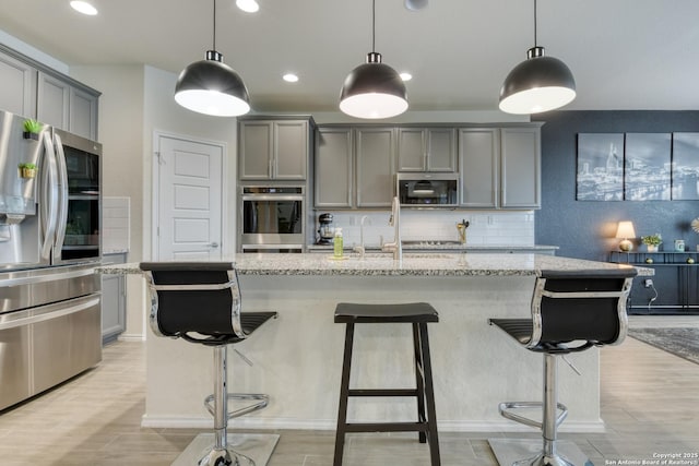 kitchen featuring appliances with stainless steel finishes, a kitchen island with sink, and pendant lighting