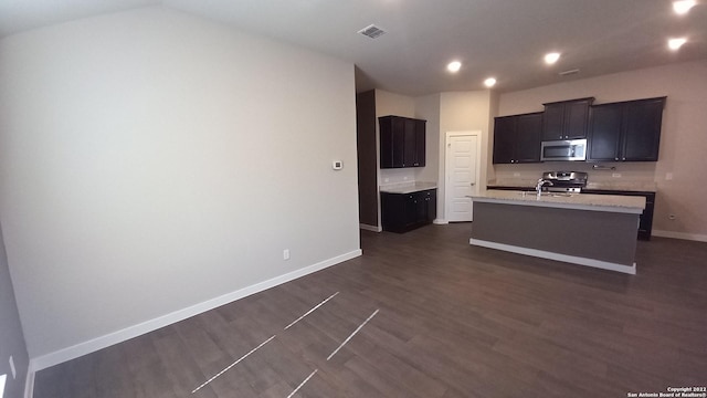 kitchen with sink, appliances with stainless steel finishes, light stone countertops, a center island with sink, and dark hardwood / wood-style flooring