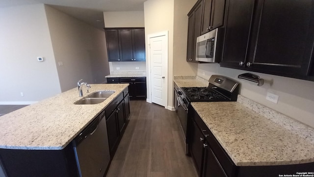 kitchen featuring dark wood-type flooring, sink, light stone counters, a center island with sink, and stainless steel appliances