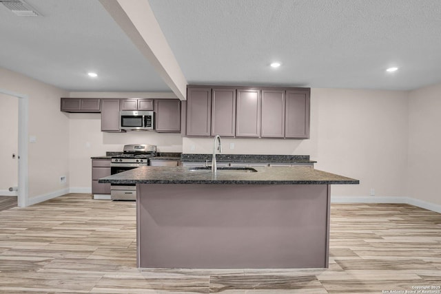 kitchen featuring stainless steel appliances, sink, an island with sink, and a textured ceiling