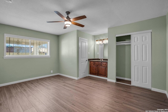 unfurnished bedroom with a closet, ensuite bath, ceiling fan, and light hardwood / wood-style flooring