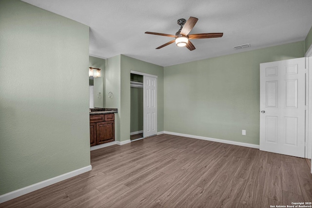 unfurnished bedroom featuring ensuite bath, light hardwood / wood-style flooring, ceiling fan, and a closet