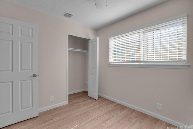 unfurnished bedroom featuring a textured ceiling, a closet, and light hardwood / wood-style flooring