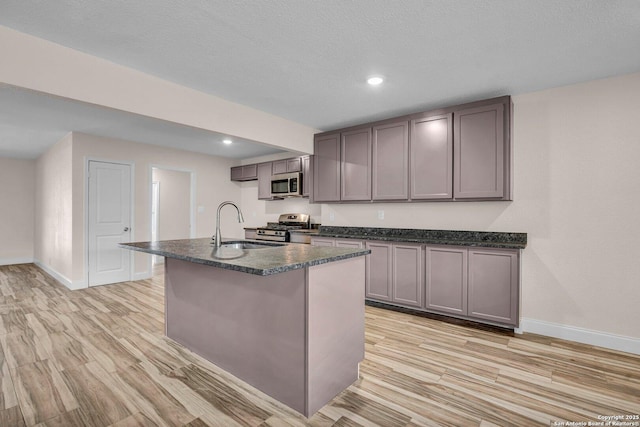 kitchen with an island with sink, sink, light wood-type flooring, stainless steel appliances, and a textured ceiling