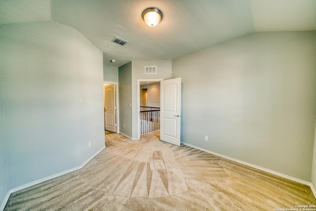 unfurnished bedroom with lofted ceiling, light colored carpet, and a textured ceiling