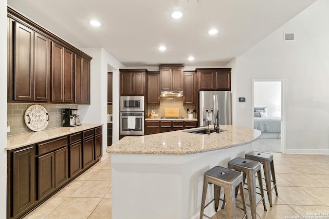 kitchen with sink, a center island with sink, light tile patterned floors, appliances with stainless steel finishes, and light stone countertops