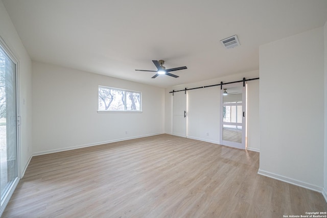 empty room featuring light hardwood / wood-style flooring, a barn door, and ceiling fan