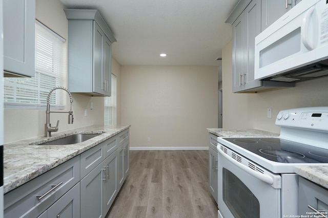 kitchen with gray cabinets, sink, light stone counters, light hardwood / wood-style floors, and white appliances