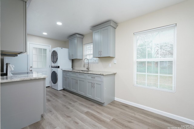 kitchen featuring light stone counters, stacked washer / dryer, sink, and gray cabinetry