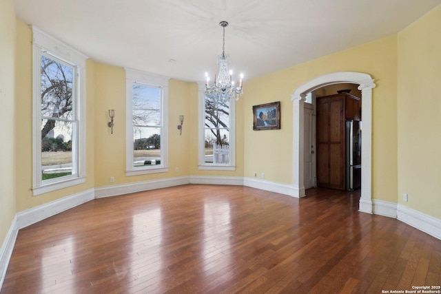 unfurnished dining area featuring arched walkways, hardwood / wood-style floors, a chandelier, and baseboards