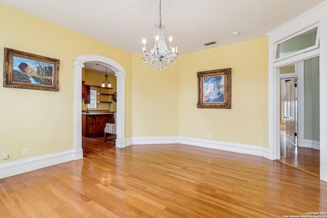 empty room featuring arched walkways, baseboards, visible vents, and light wood-style floors