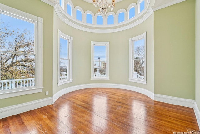 spare room with hardwood / wood-style flooring, baseboards, a wealth of natural light, and a notable chandelier