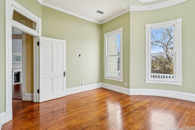 spare room with crown molding, wood-type flooring, visible vents, a fireplace with flush hearth, and baseboards