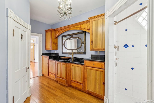 kitchen featuring a notable chandelier, a sink, light wood-type flooring, brown cabinets, and dark stone countertops