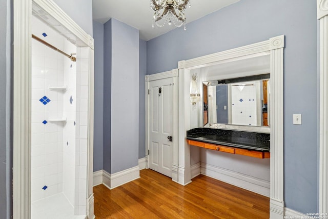 full bathroom with a tile shower, wood finished floors, vanity, and baseboards