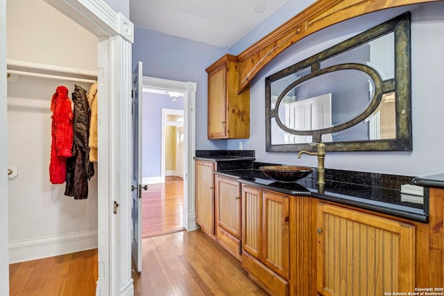 kitchen featuring brown cabinetry, a sink, light wood-style flooring, and baseboards