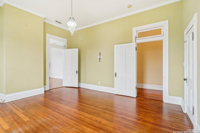 empty room with visible vents, baseboards, hardwood / wood-style floors, an inviting chandelier, and crown molding