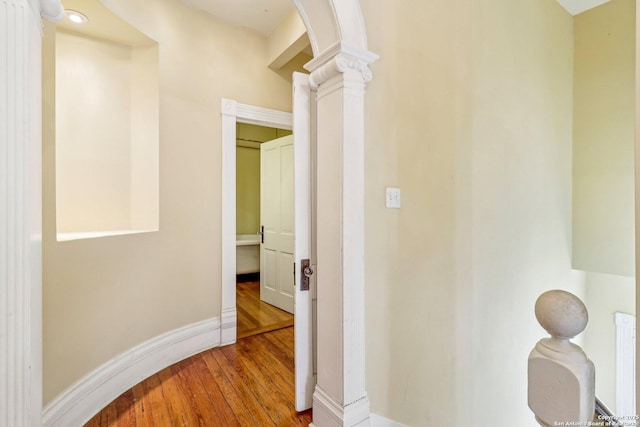 hall with arched walkways, baseboards, ornate columns, and wood finished floors