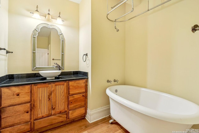 bathroom featuring a soaking tub, vanity, baseboards, and wood finished floors