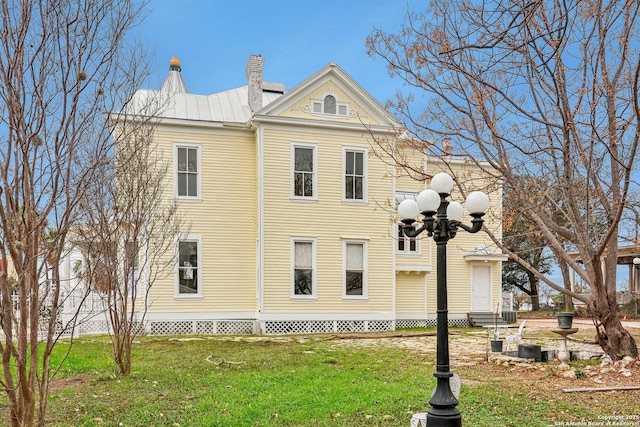 view of property exterior with entry steps, a yard, a chimney, and metal roof