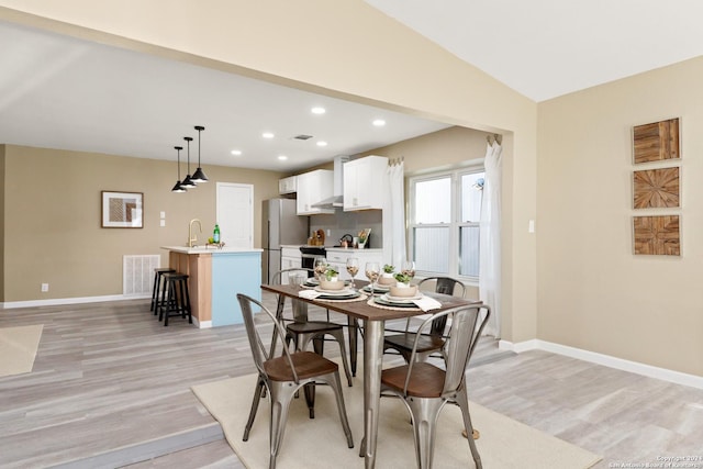 dining space with sink, light hardwood / wood-style flooring, and vaulted ceiling