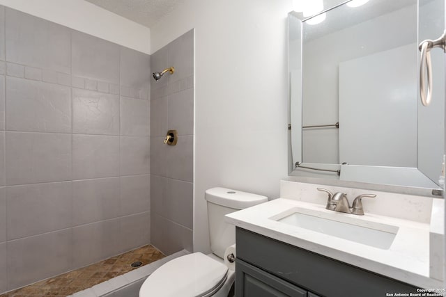 bathroom featuring vanity, a tile shower, a textured ceiling, and toilet