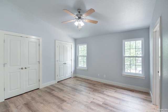 unfurnished bedroom with lofted ceiling, ceiling fan, light hardwood / wood-style floors, and multiple closets