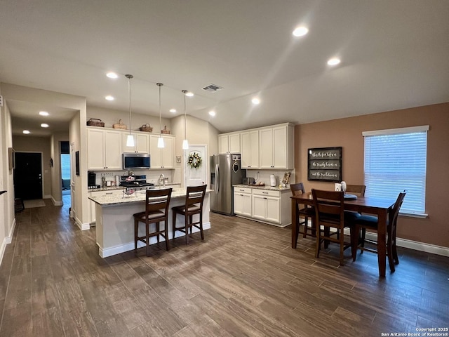 kitchen with pendant lighting, white cabinetry, stainless steel appliances, and a center island with sink