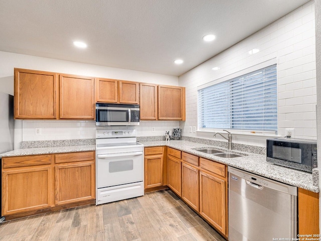 kitchen with stainless steel appliances, light stone countertops, sink, and light wood-type flooring