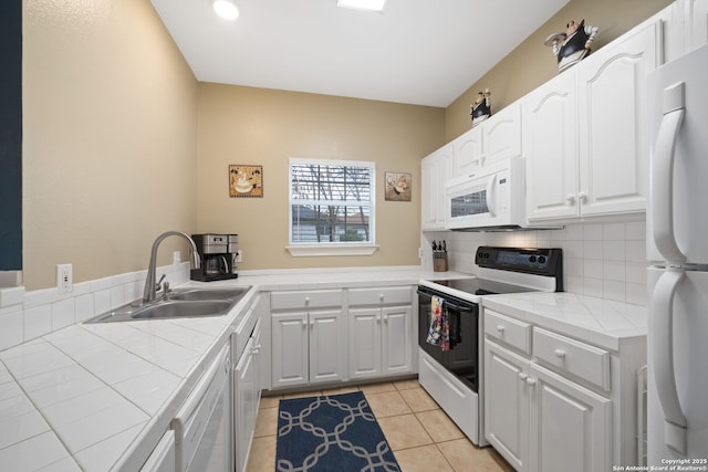 kitchen with sink, white appliances, light tile patterned floors, tile counters, and kitchen peninsula