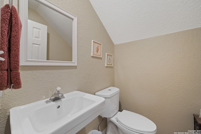 bathroom featuring toilet, sink, vaulted ceiling, and a textured ceiling