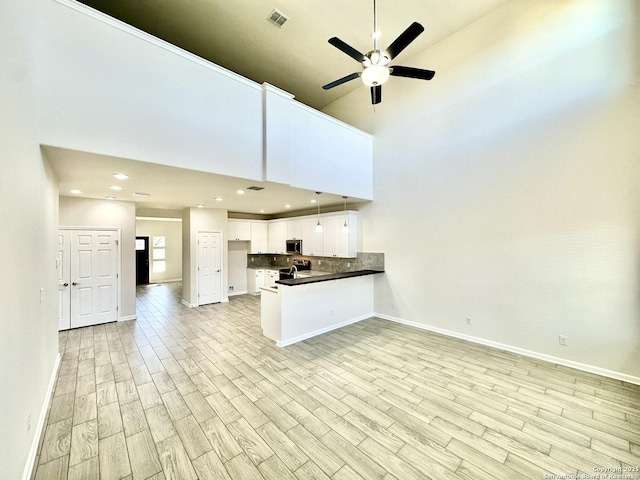 kitchen featuring kitchen peninsula, white cabinets, stainless steel appliances, light hardwood / wood-style floors, and a high ceiling