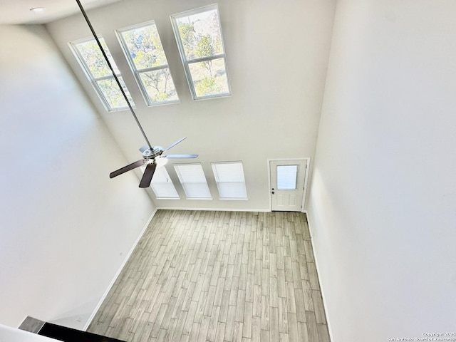 unfurnished living room featuring ceiling fan, a high ceiling, and light wood-type flooring