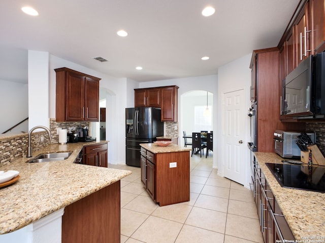 kitchen featuring sink, a center island, light stone counters, black appliances, and decorative backsplash