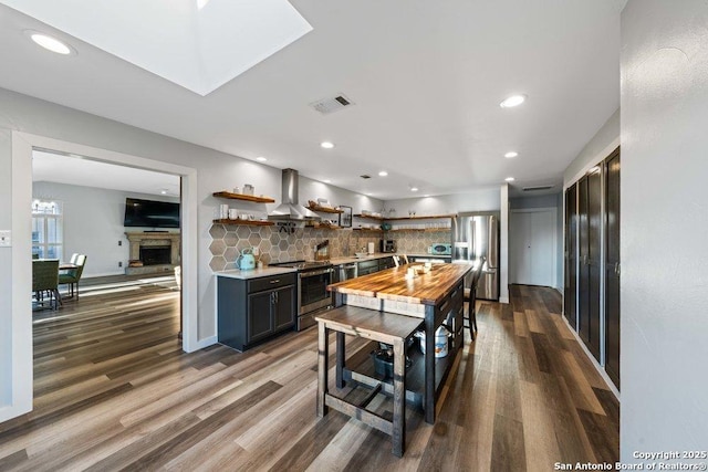 kitchen with wooden counters, appliances with stainless steel finishes, dark hardwood / wood-style floors, decorative backsplash, and wall chimney range hood