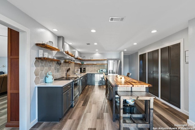 kitchen featuring island exhaust hood, appliances with stainless steel finishes, light wood-type flooring, and backsplash